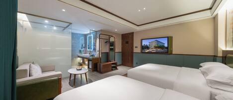A hotel room with two beds, a sofa, a small table, a mirror, and a TV on the wall.