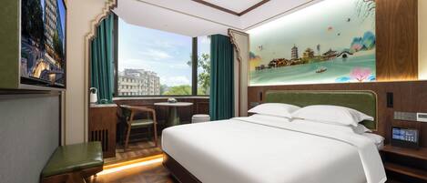 A hotel room with a large bed, a desk, and a view of a cityscape through the window.