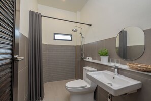 A modern bathroom with a shower, toilet, sink, and a small window.