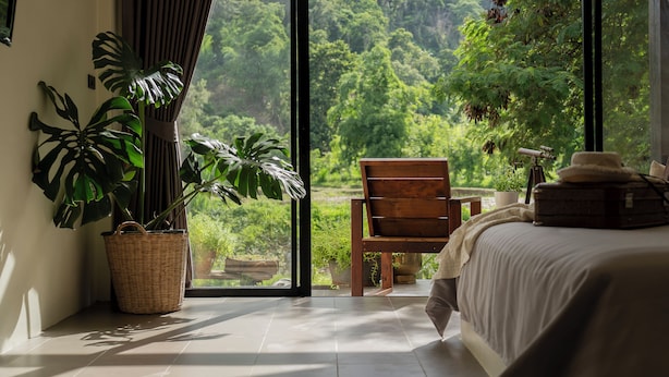 Een slaapkamer met een groot raam, een houten stoel, een bed en een koffer.