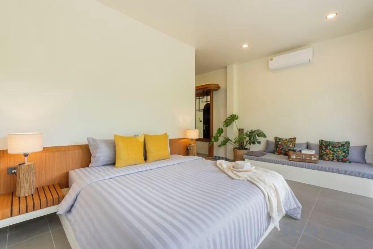 A hotel room with a large bed, bedside lamps, a sofa, and a potted plant.