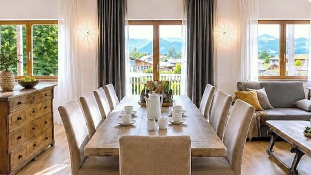 A dining area with a long table set for four, a sofa, and a dresser.