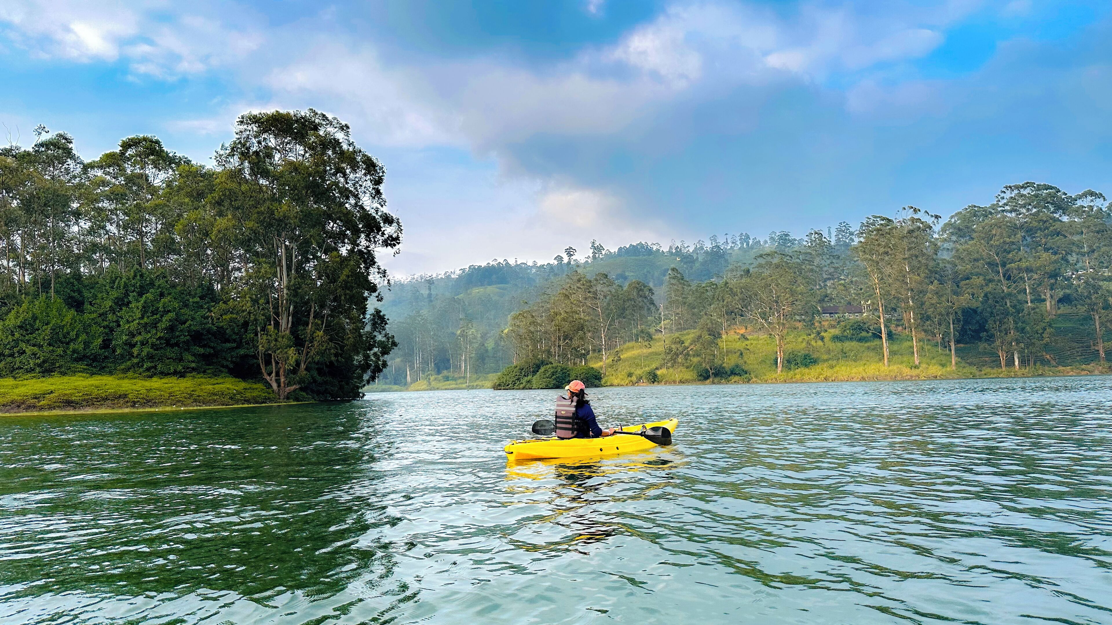 Una persona remando en kayak por un río tranquilo rodeado de un bosque denso y colinas.