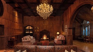 A cozy, wood-paneled room with a large, ornate chandelier, a fireplace, and comfortable seating. - Uga Halloowella - Hatton - All Inclusive (Norwood)