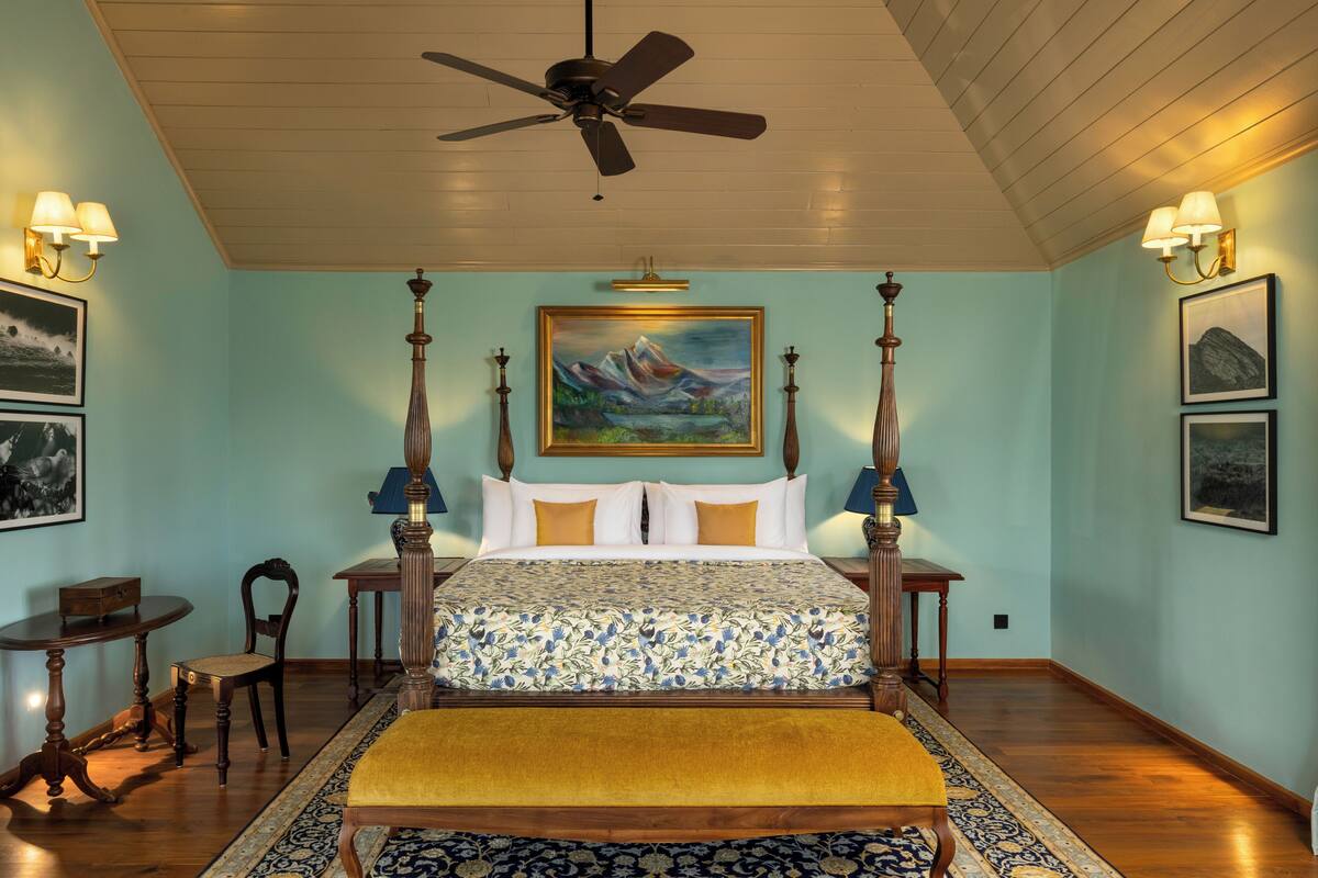 A bedroom with a four-poster bed, a ceiling fan, a painting above the bed, and a small table with chairs.