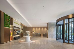 A modern hotel lobby with a reception desk, a green wall with plants, and a large window. - Home2 Suites BY Hilton Kunming Xishan (KUNMING)