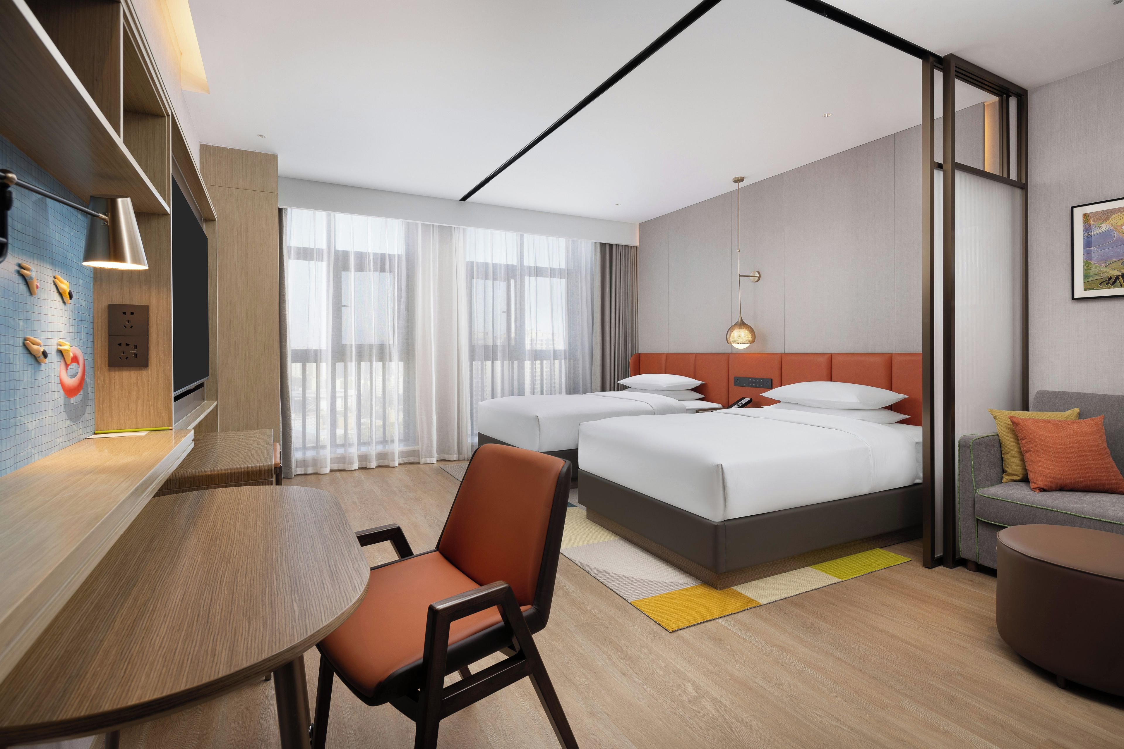 A modern hotel room with a bed, a desk, and a seating area.
