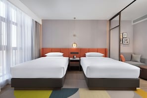 Una habitación de hotel con dos camas, un sofá, una mesita de noche y un ventanal con cortinas.