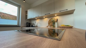 A modern kitchen with a reflective countertop, built-in appliances, and a window with blinds.