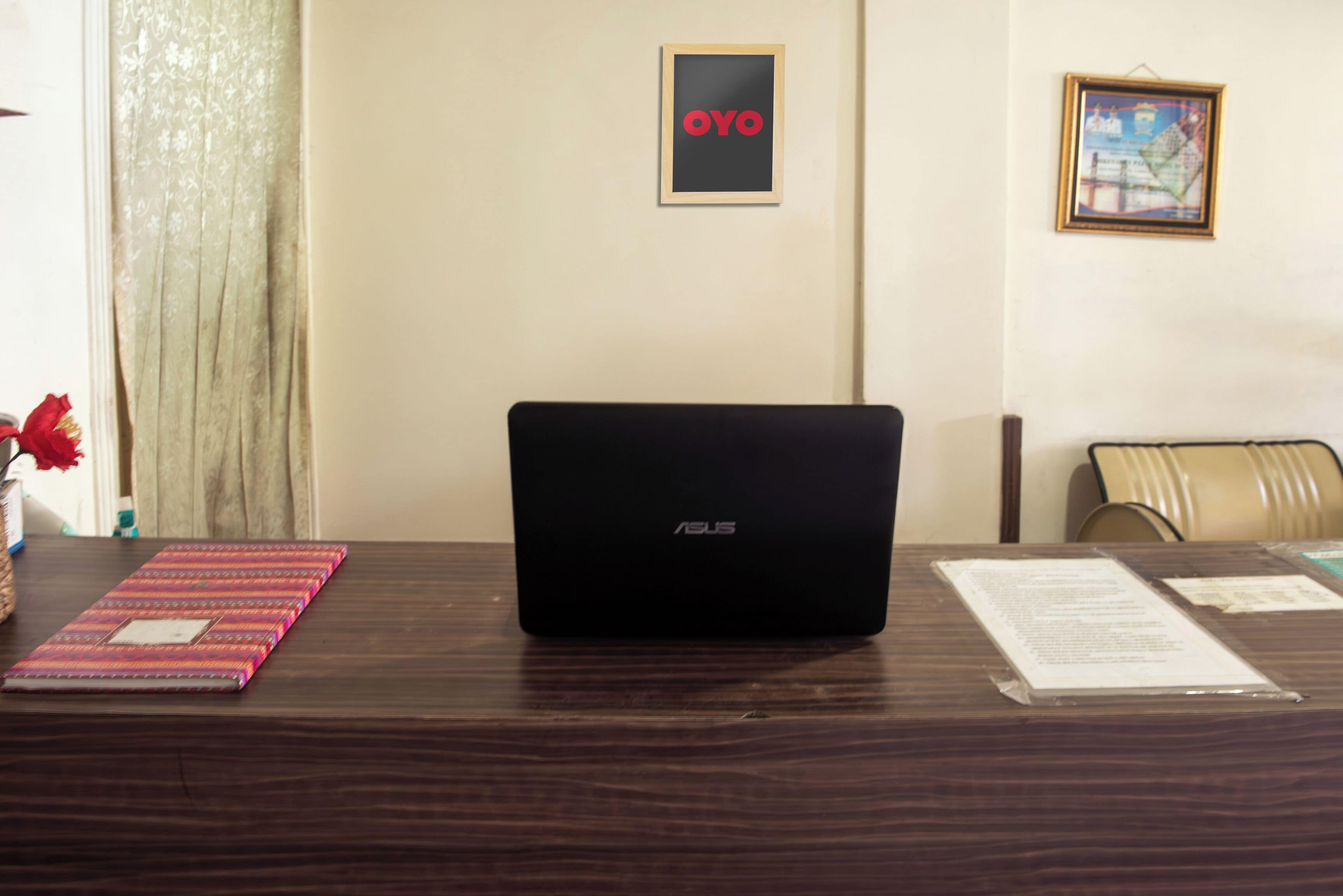 A laptop on a desk with a framed sign reading "OYO" and a framed picture on the wall.