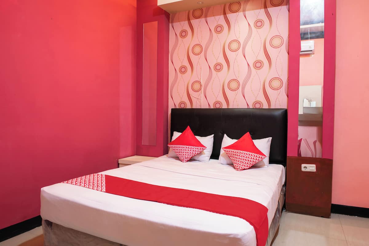 A neatly made bed with red and white bedding, a black headboard, and patterned wallpaper.