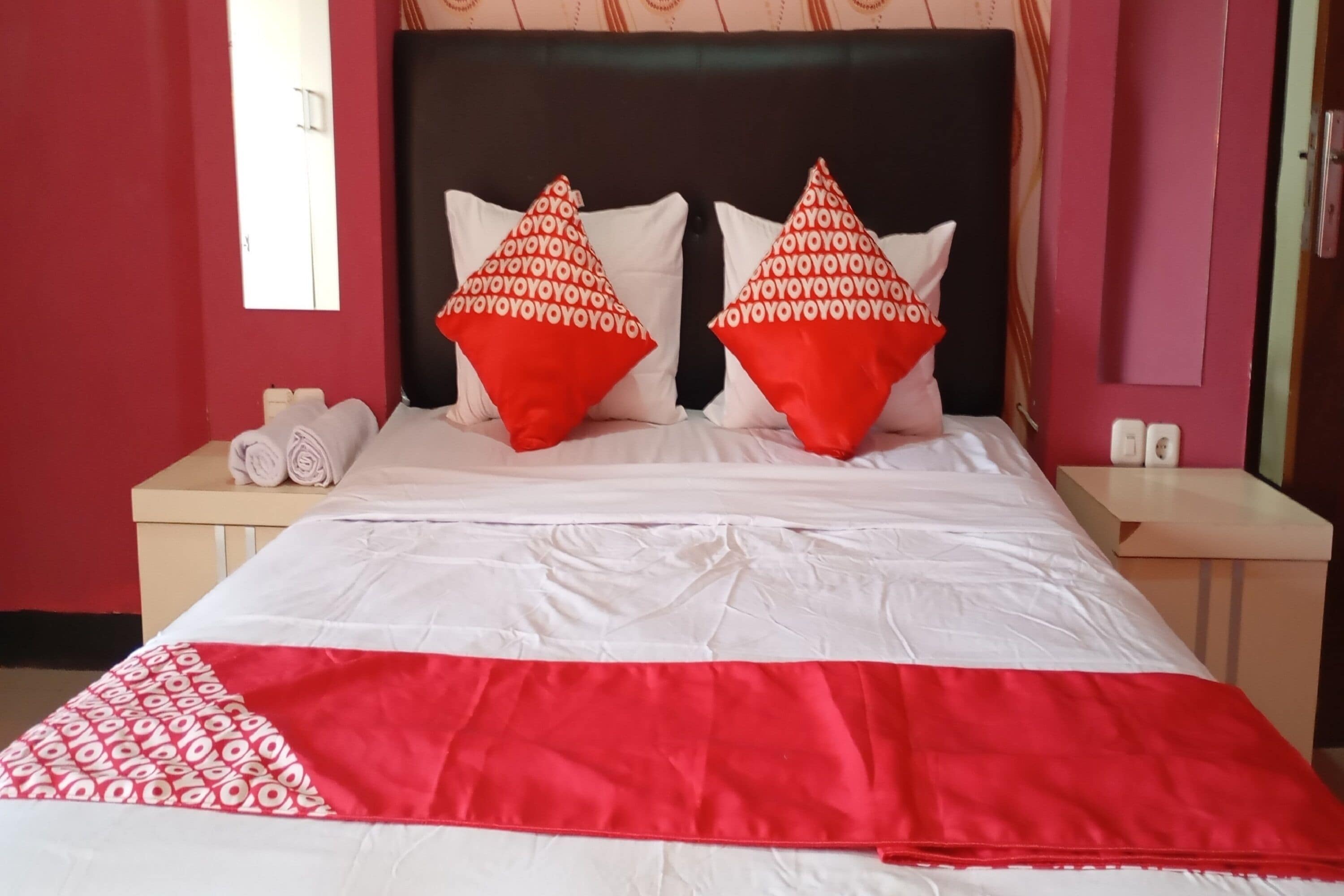 A neatly made bed with white and red bedding, two red pillows with a pattern, and a red and white throw at the foot of the bed.