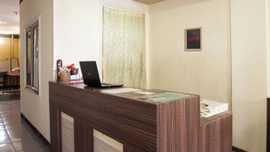 Un comptoir d’accueil avec un ordinateur portable, une enseigne encadrée portant le logo « OYO », et une fenêtre avec des rideaux.