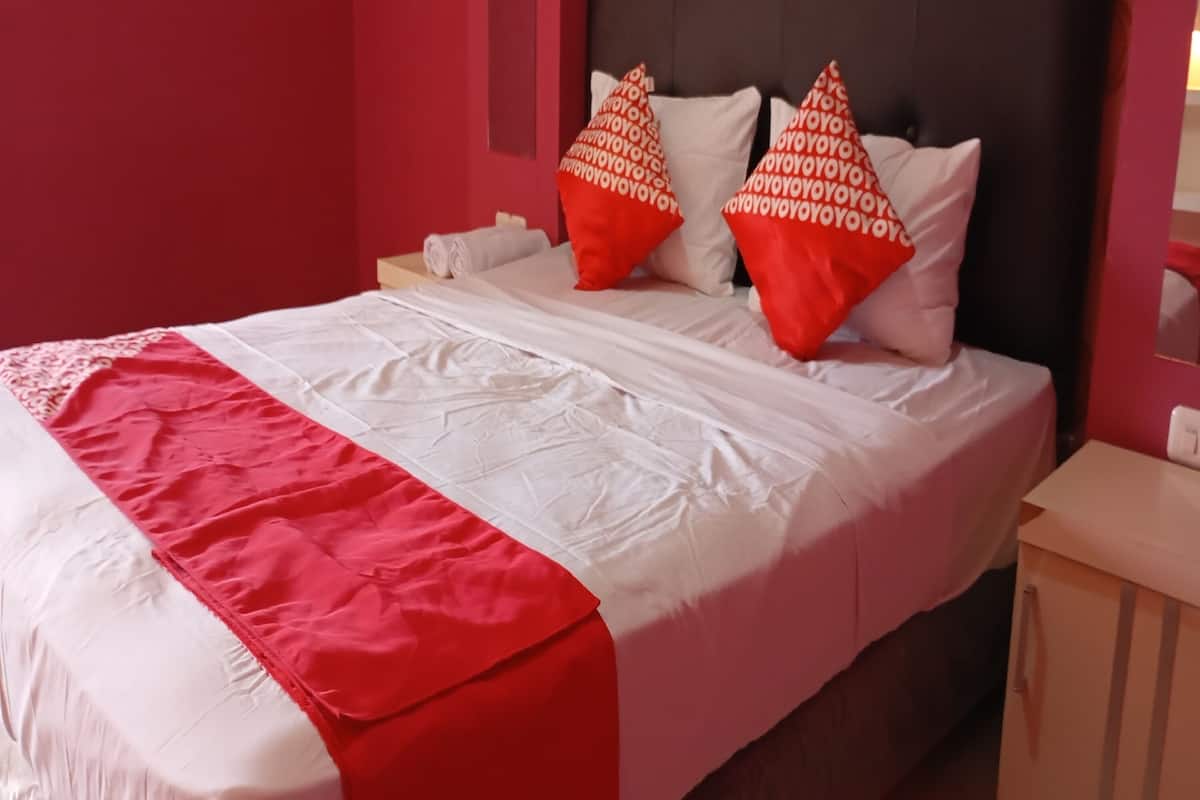 A neatly made bed with white and red bedding, two red pillows with white text, and a wooden nightstand with a lamp.