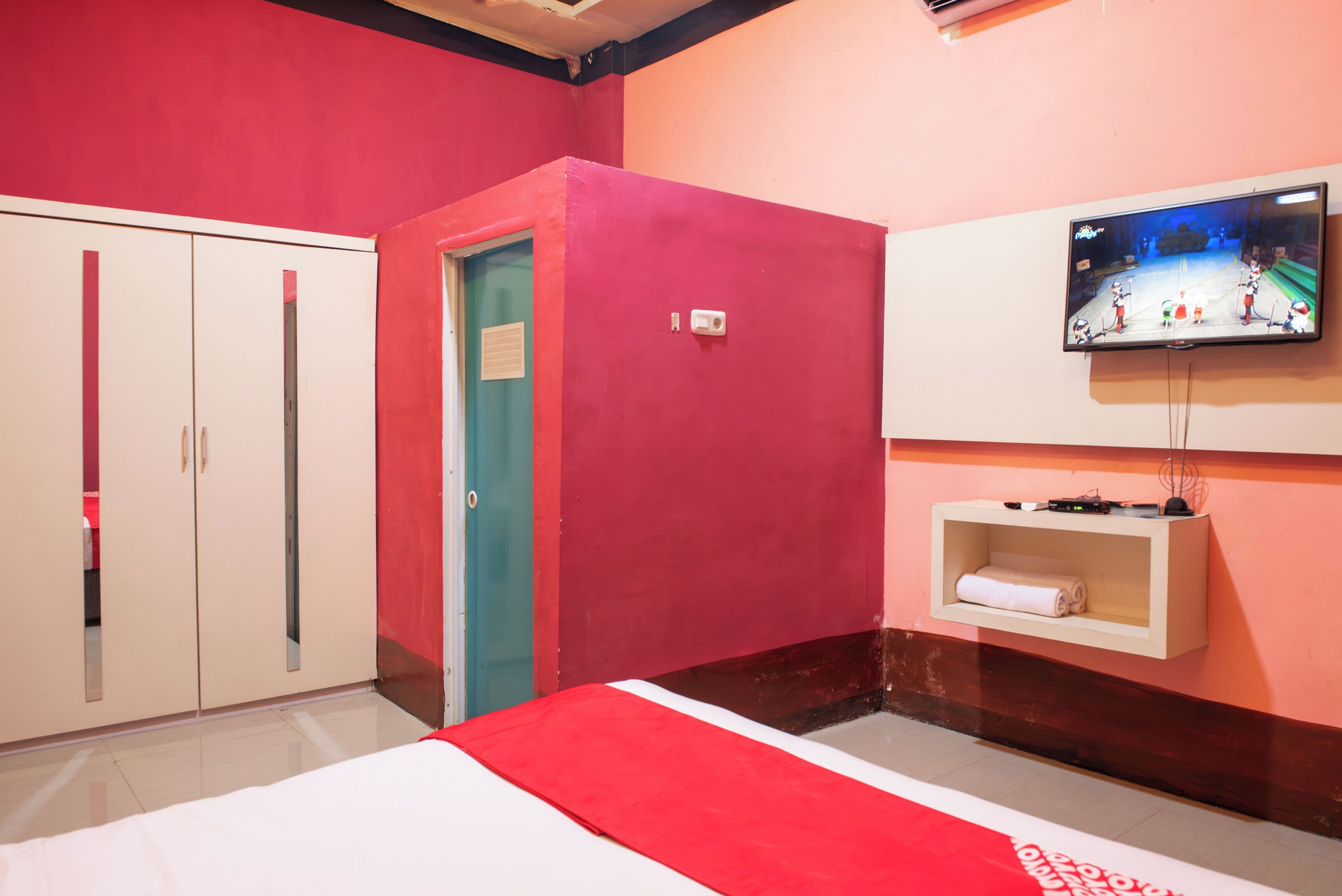 A hotel room with a bed, a wardrobe, a television mounted on the wall, and a small shelf with a towel.