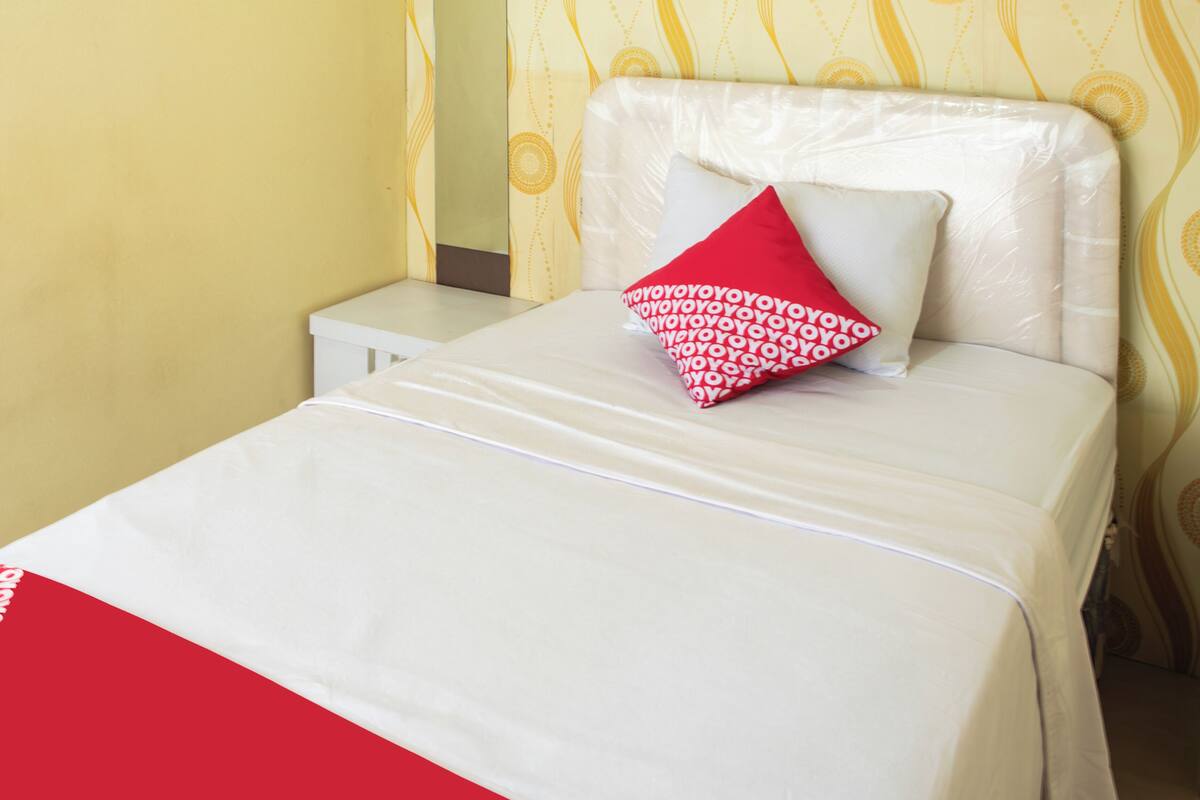 A neatly made bed with a white mattress and a red and white patterned pillow.