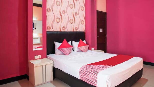 Une chambre moderne avec un grand lit, des murs roses et une tête de lit à motifs.