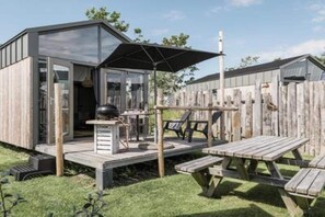 A wooden cabin with a glass door, a barbecue grill, and a picnic table.