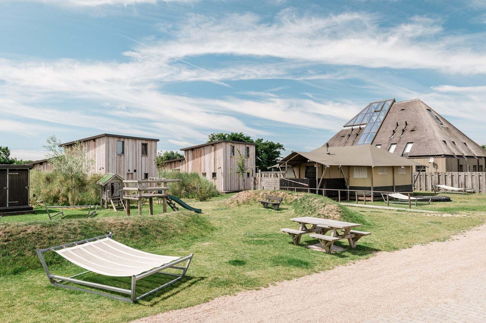 A rustic outdoor setting with wooden cabins, picnic tables, and a hammock.