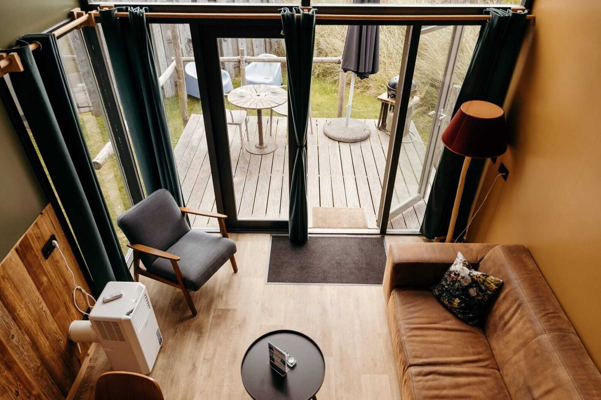 A cozy room with a wooden floor, a sofa, a chair, a small table, and a large window with curtains.