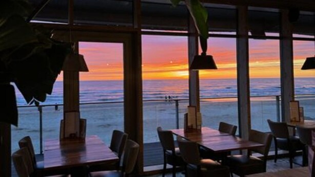A restaurant with large windows overlooking the ocean at sunset.