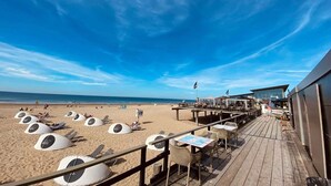 A beachside restaurant with outdoor seating, including tables and umbrellas, overlooking the ocean.