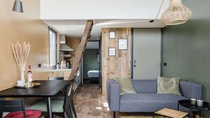 A modern living room with a grey sofa, a wooden accent wall, and a dining area with a dark table and chairs.