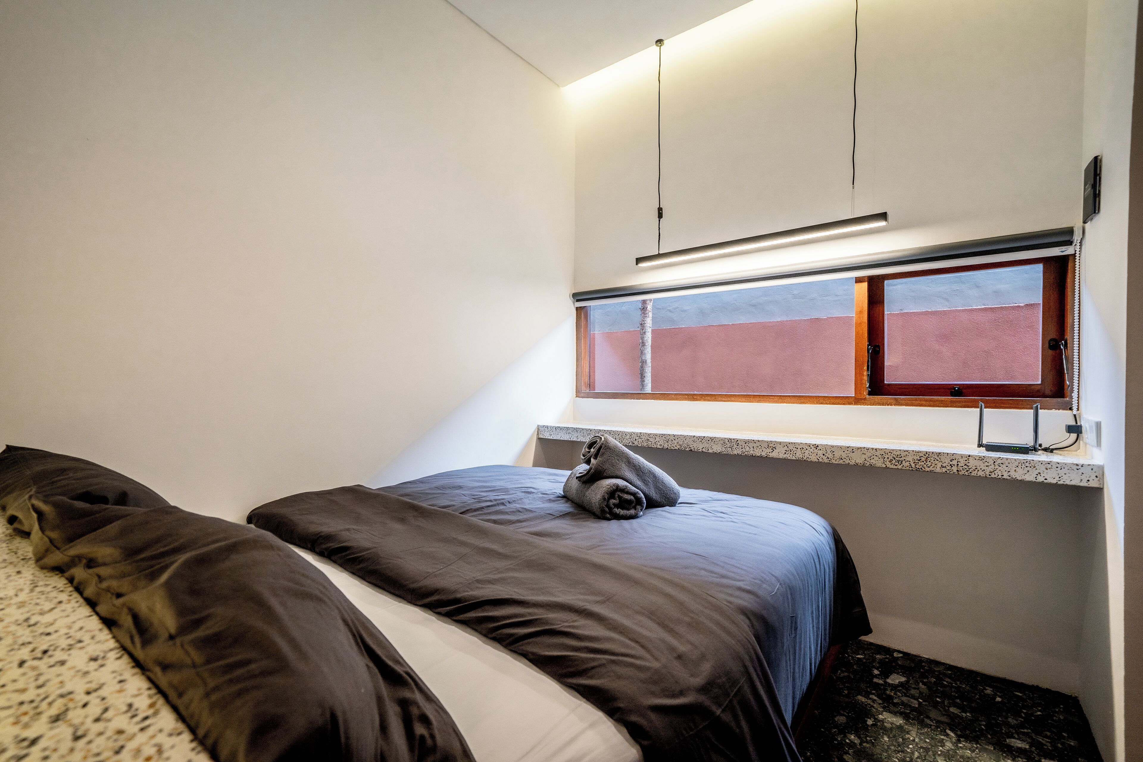 Um quarto pequeno e moderno, com uma cama, janela e luminária no teto.