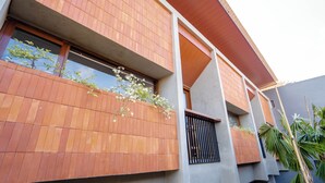 A modern building with a flat roof, large windows, and a balcony with plants. - Kumiko Apartment (Canggu)