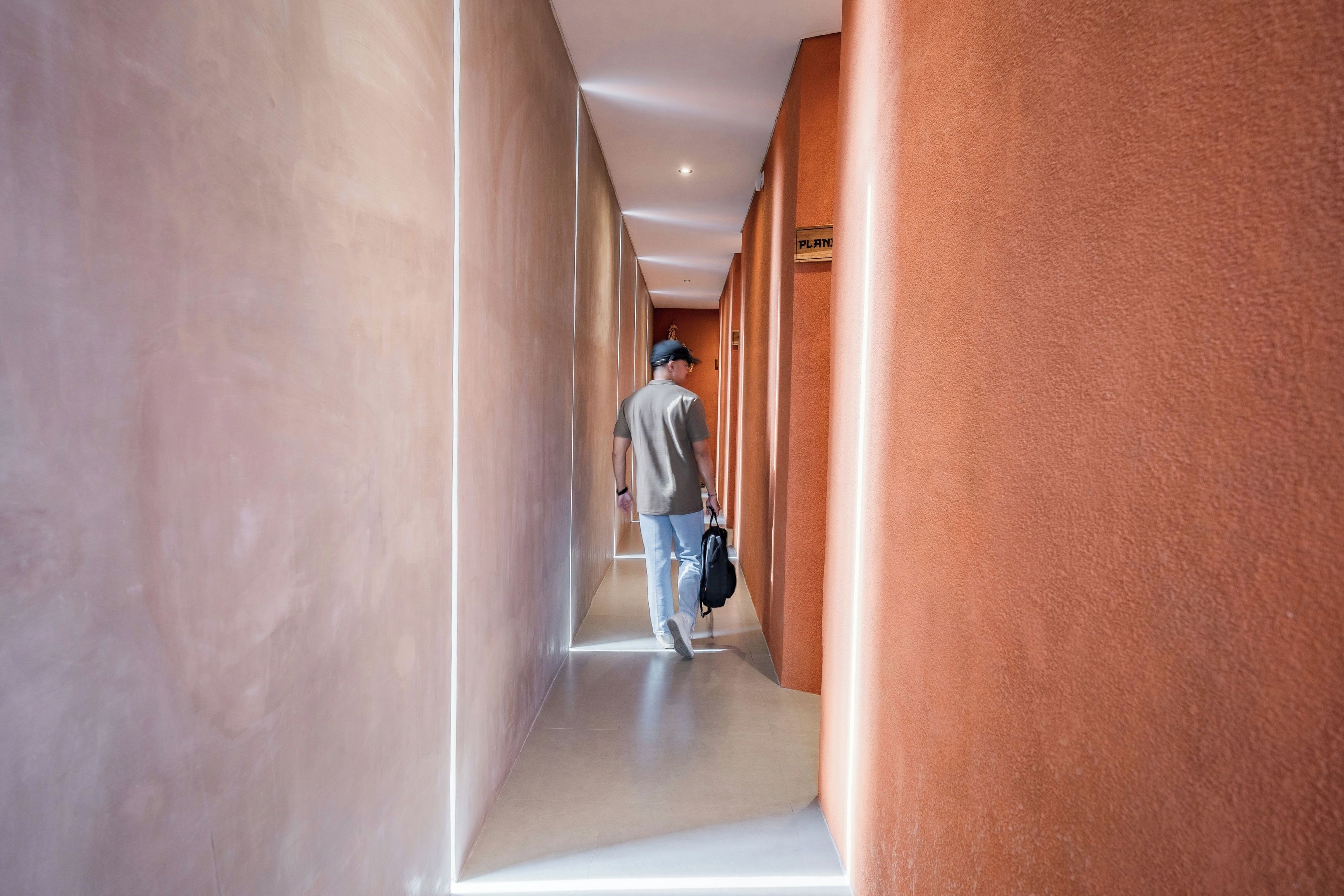 A corridor with a person walking, walls with a sign reading "PLAN", and a ceiling with recessed lighting.