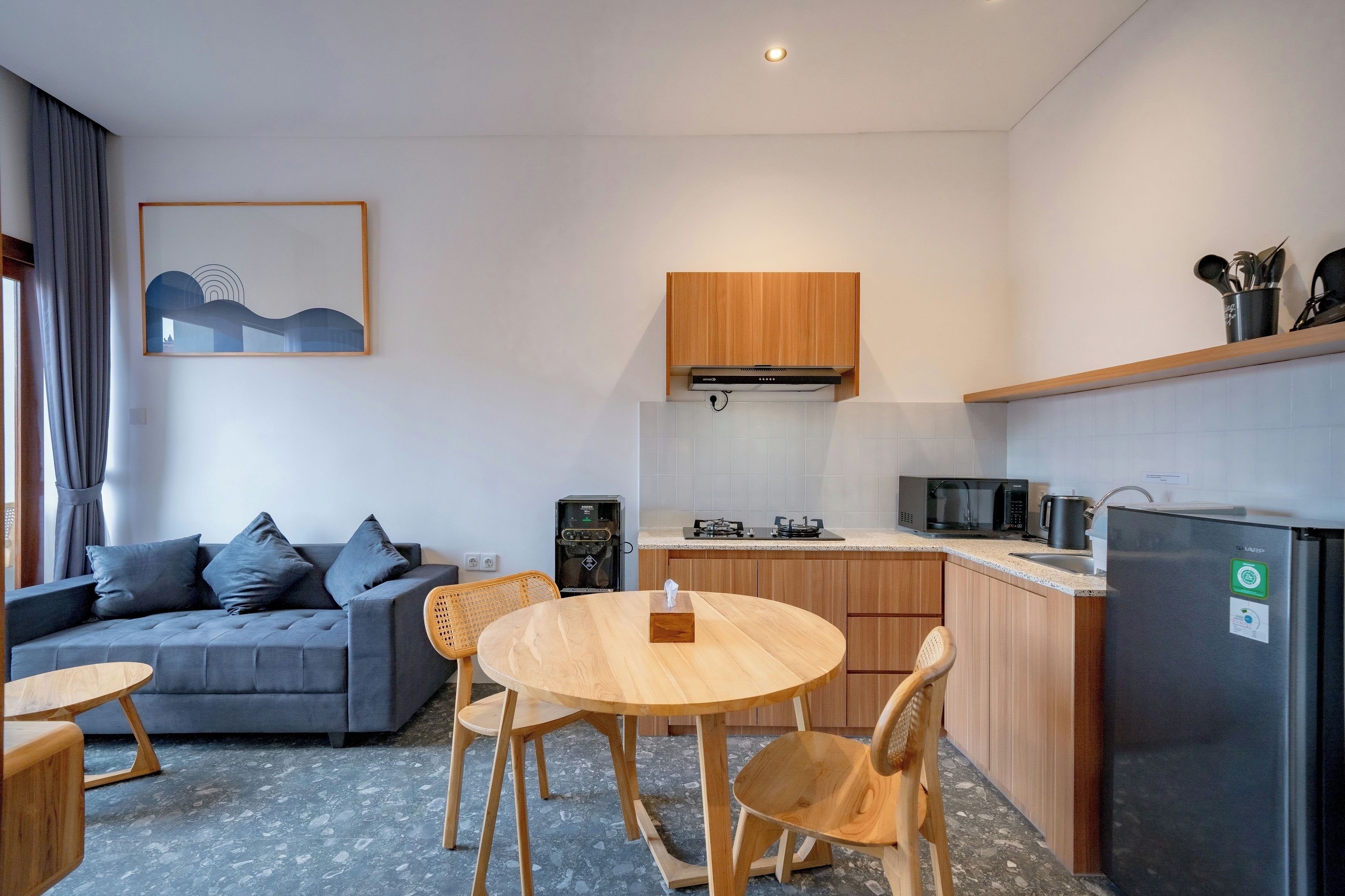 A modern kitchen with a dining area, grey sofa, and wooden chairs.