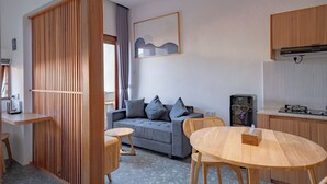 A modern living room with a grey sofa, wooden accents, a dining table, and a kitchen area with a water dispenser. - Kumiko Apartment (Canggu)