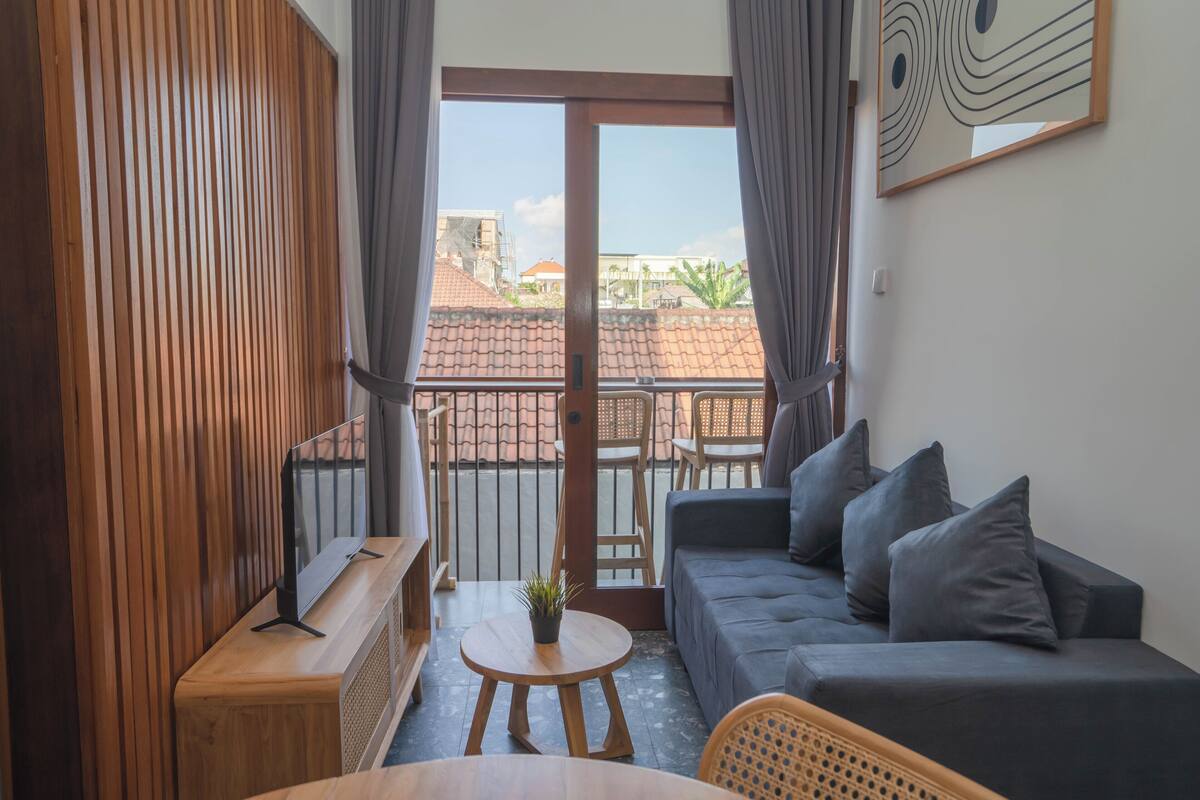 Ein Balkon mit Holzboden, einem grauen Sofa und einem kleinen Tisch mit einer Pflanze.