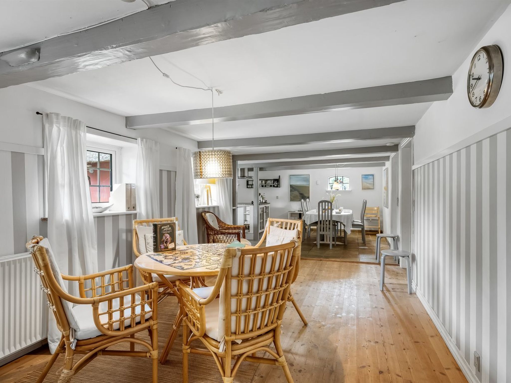 A dining area with a round table and wicker chairs, a hanging light fixture, and a clock on the wall.