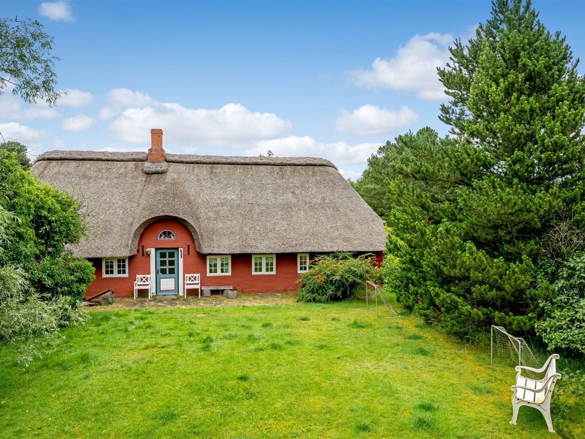 A traditional thatched-roof house with a red exterior, a blue door, and a small porch with white railings.