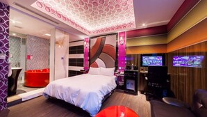 Ein modernes Hotelzimmer mit einem großen Bett, einem roten Hocker, einem Fernseher und einer Spielkonsole.