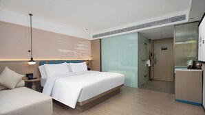 Habitación de hotel moderna con cama, mesita de noche, lámpara y vista al pasillo.