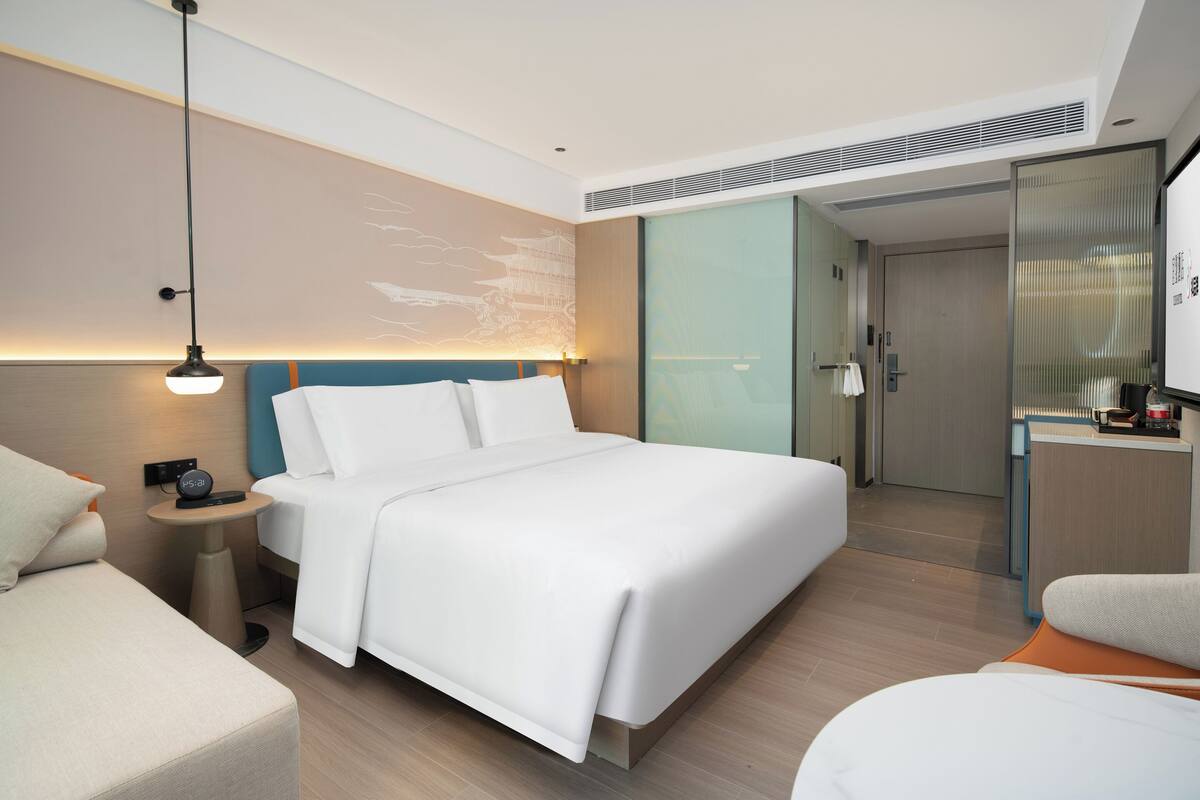 Habitación de hotel moderna con una cama grande, mesitas de noche, un escritorio y una puerta corredera al baño.
