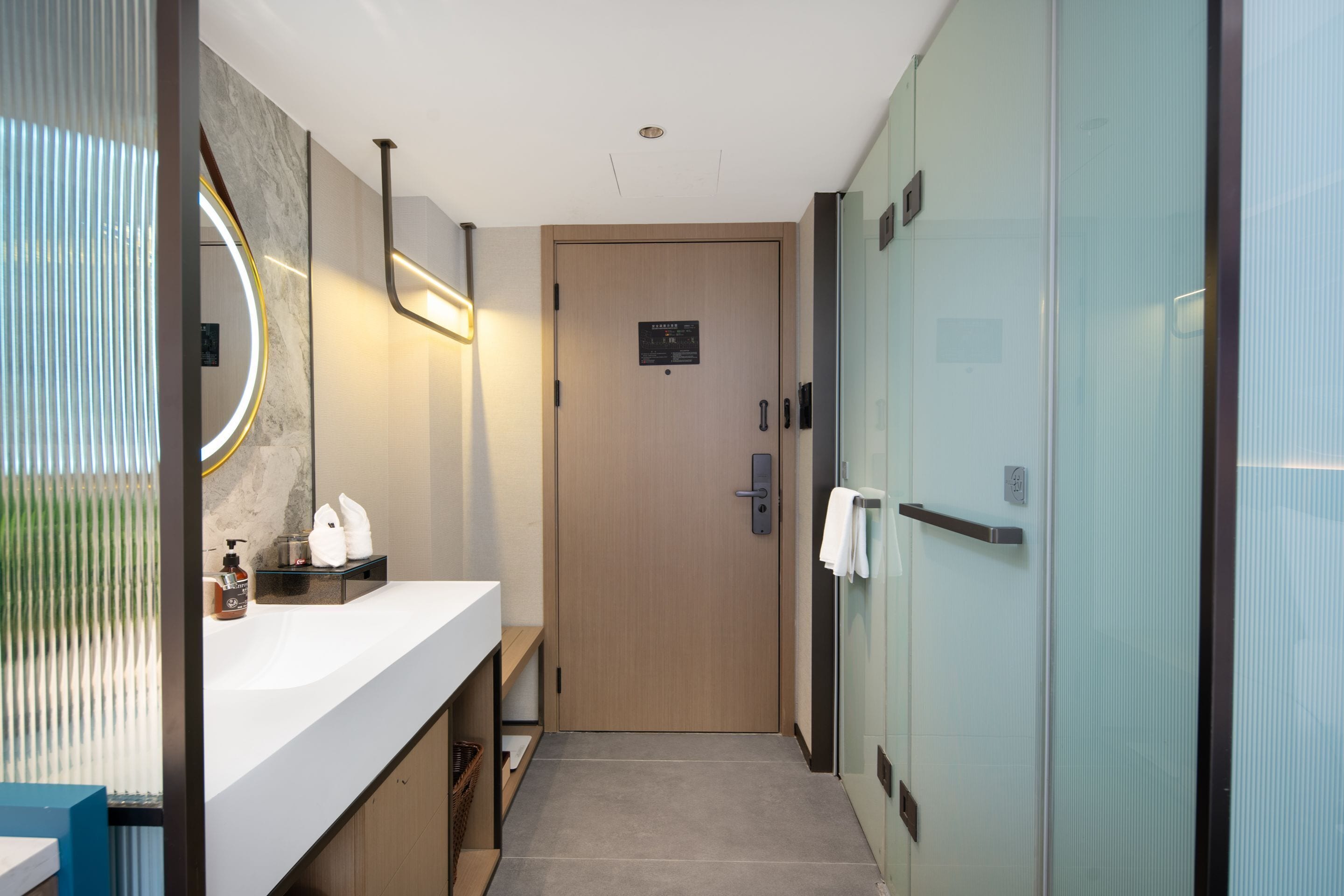 A modern bathroom with a marble vanity, a glass shower enclosure, and a wooden door.