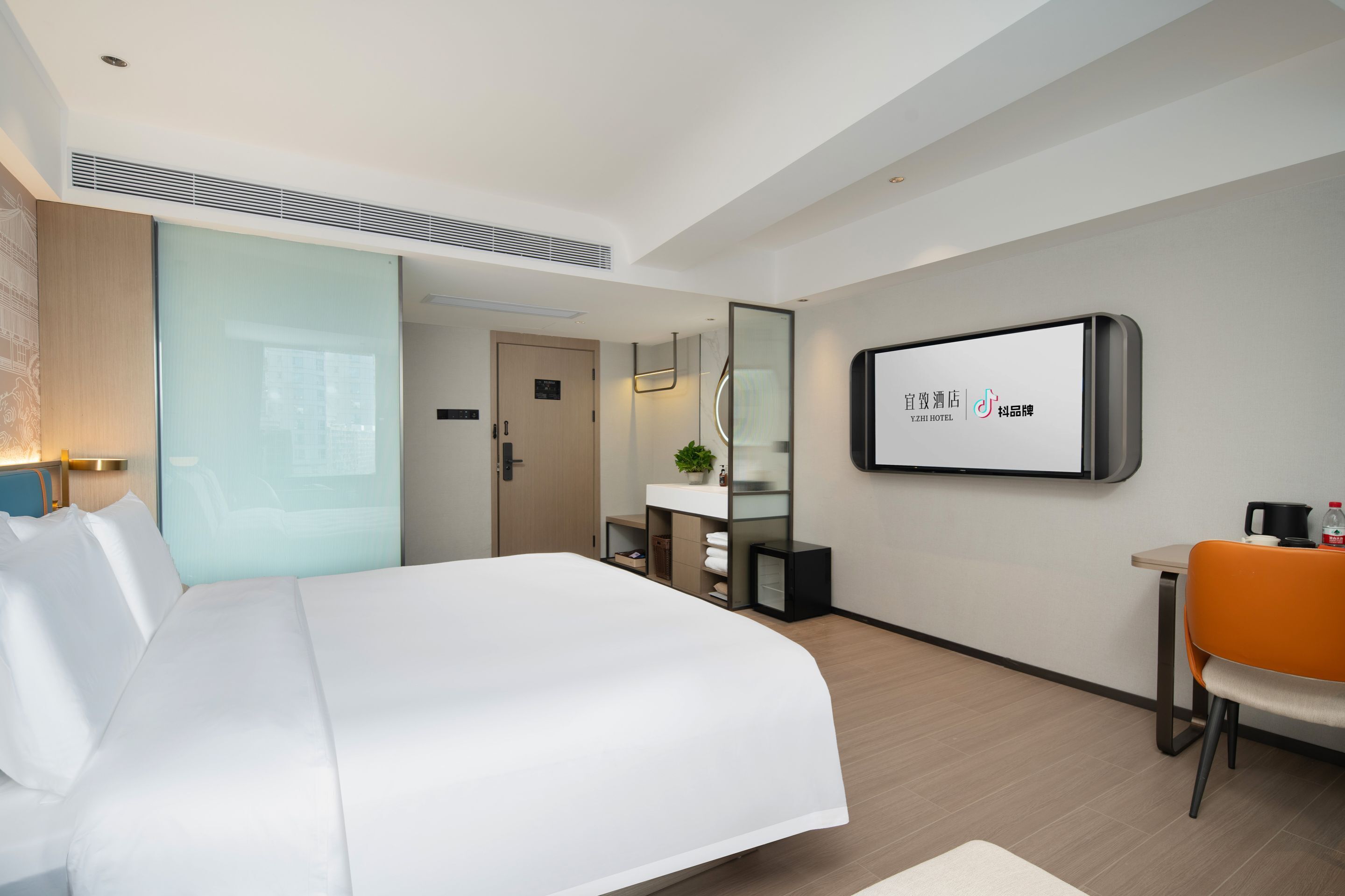 A modern hotel room with a large bed, a desk with a chair, a mirror, and a television on the wall.