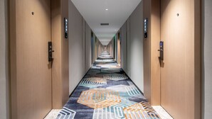 Un pasillo de hotel con alfombra estampada, puertas de madera y un panel de control de ascensor digital.