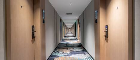 A hotel hallway with a patterned carpet, wooden doors, and a digital elevator control panel.