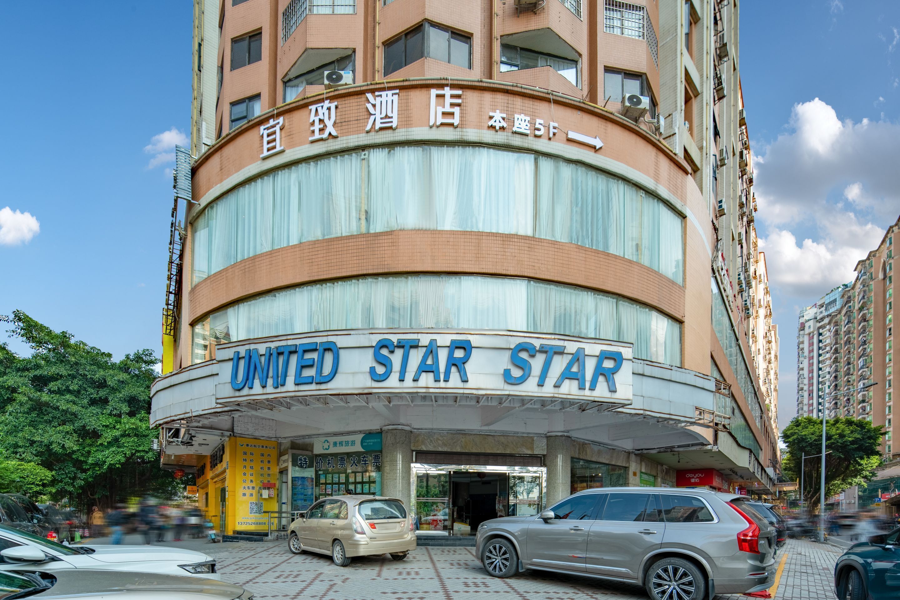 Un hôtel à plusieurs étages, doté d’une façade incurvée, d’une enseigne indiquant « UNITED STAR STAR » et d’une entrée bien visible, avec des voitures garées devant.