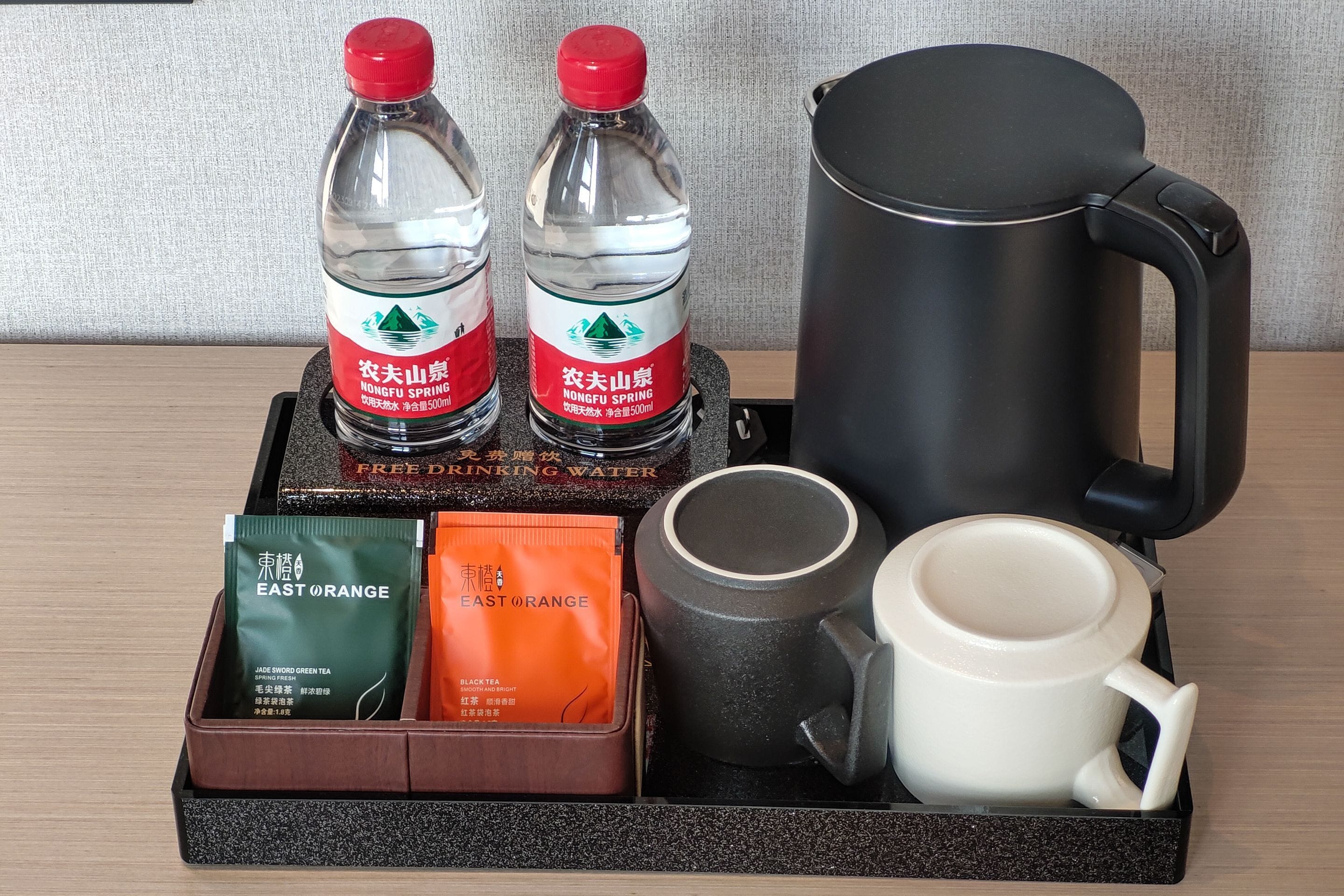 A tray with two water bottles, a black thermos, two tea packets, and a white mug.