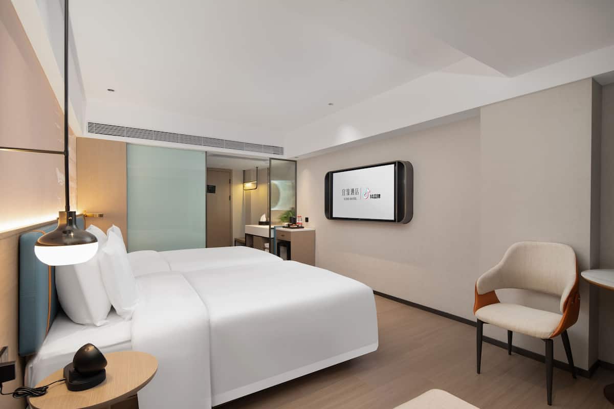 Una habitación de hotel moderna con una cama grande, un escritorio, una silla y un televisor de pantalla plana en la pared.