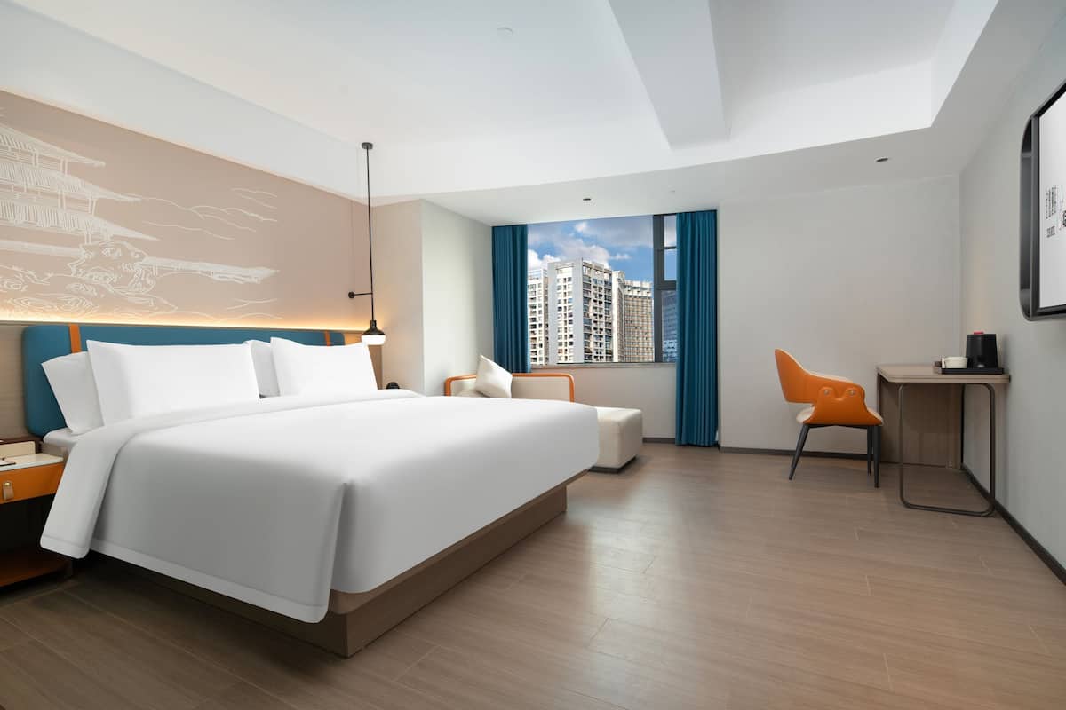 Una habitación de hotel moderna con una cama grande, un escritorio y una silla. Hay una ventana con vistas a edificios altos.
