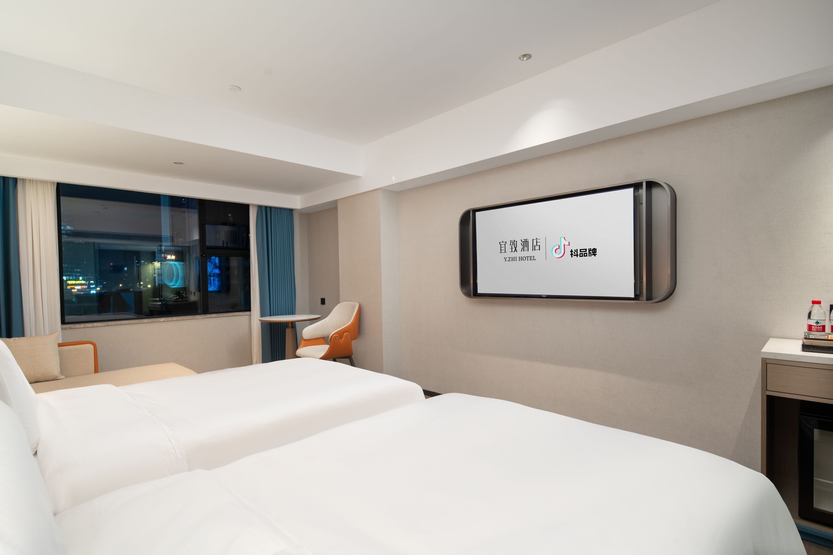 Een hotelkamer met twee bedden, een aan de muur bevestigde televisie, een tafeltje en een stoel.
