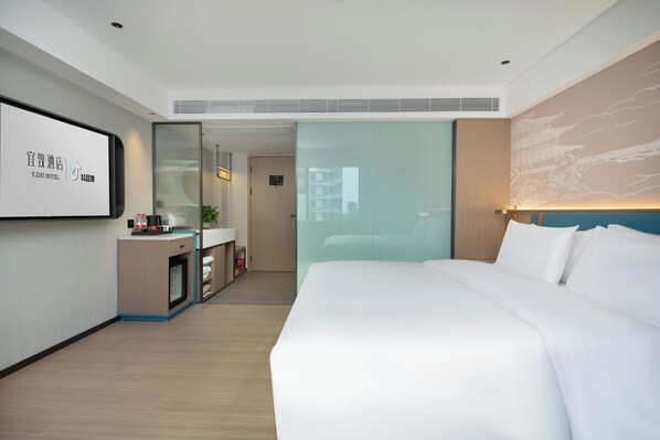 Una habitación de hotel moderna con una cama grande, un escritorio con una computadora y un separador de vidrio que divide la habitación del pasillo.