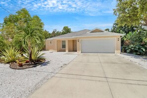 A single-story house with a garage, surrounded by a gravel driveway and various plants. - PRIVATE HEATED POOL | SCREENED LANAI & BBQ | SPLIT FLOOR PLAN | UNDER 2 MILES TO BONITA BEACH (Bonita Springs)