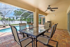 A covered patio with a glass table and chairs, a ceiling fan, and a view of a swimming pool and backyard. - PRIVATE HEATED POOL | SCREENED LANAI & BBQ | SPLIT FLOOR PLAN | UNDER 2 MILES TO BONITA BEACH (Bonita Springs)